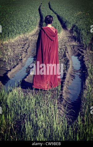 Una donna in red cape in piedi su un fiel nel fango Foto Stock