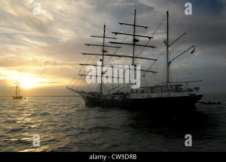 Una tre masted sailing ship semi stagliano contro il sole di setting. Cielo nuvoloso, sole che tramonta dietro le nuvole. Foto Stock