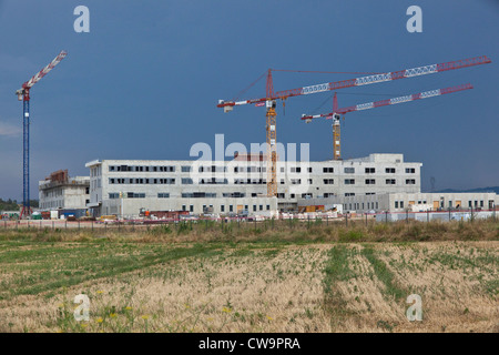 Un grande edificio sito con tre gru alti nel paesaggio suburbano Foto Stock