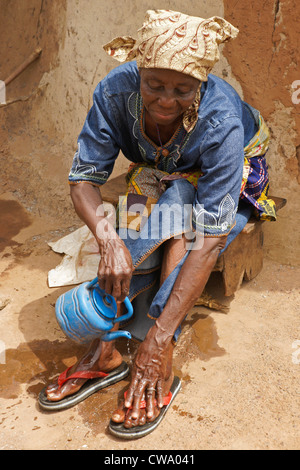Donna lavando i suoi piedi fuori capanna di fango, Gambaga, Ghana Foto Stock