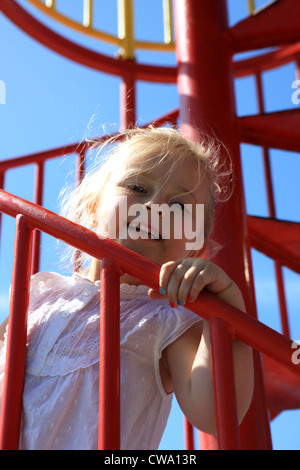 Tre anni ragazza bionda salire le scale di uno scivolo al parco giochi Foto Stock