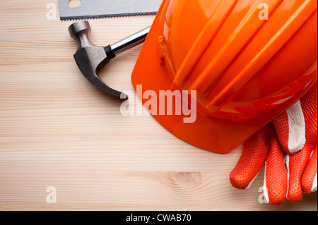 Hardhat, guanti e alcuni attrezzi assortiti disposto su una superficie di legno. Costruzione, riparazione o miglioramento di casa dello sfondo. Foto Stock