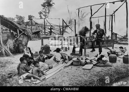 Del Vietnam del Sud la donna e i bambini seduti in mezzo alle rovine del loro villaggio, bruciato dalle truppe governative sul sospetto di essere un Viet Foto Stock