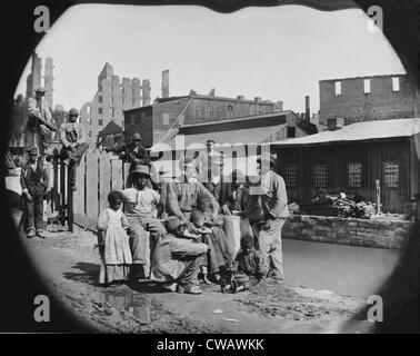 Un recentemente liberato americano africano gruppo di uomini e un paio di bambini che presentano da un canale contro le rovine di Richmond, Virginia. Foto Stock