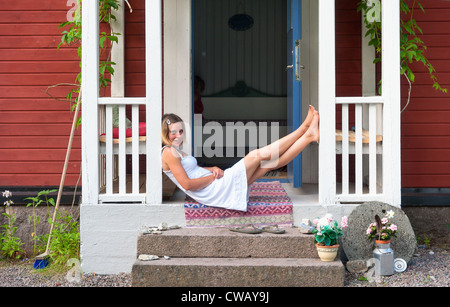 Attraente donna seduta su una veranda di svedese di casa in legno, Foto Stock