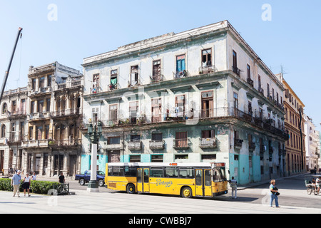 Edifici e pullman giallo nella parte anteriore di una corsa verso il basso del blocco di appartamenti nel centro di Havana, Cuba Foto Stock