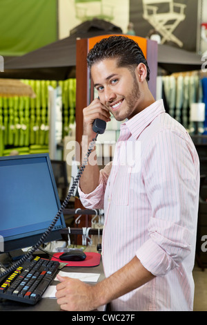 Ritratto di un addetto alle vendite felici ascoltando ricevitore telefonico in negozio Foto Stock