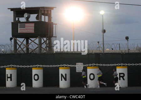 Femmina di Polizia Militare jog passato una torre di guardia con un prominente bandiera americana e le barriere che esplicitino onore a Camp Delta Foto Stock