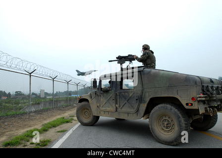 Noi Airman custodisce il perimetro di base dalla pistola torretta di un Humvee mentre un F-16 Fighter Aircraft terre in background. A Foto Stock