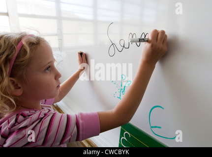 7 anno vecchia ragazza practice iscritto il suo nome in corsivo su una lavagna bianca Foto Stock