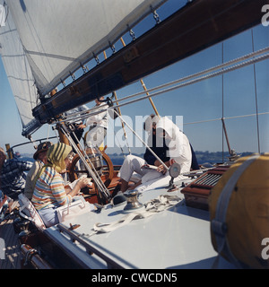 Presidente e Jacqueline Kennedy in barca a vela con i suoi genitori, Janet e Hugh Auchincloss. Jackie Kennedy è il fumo e la lettura Foto Stock
