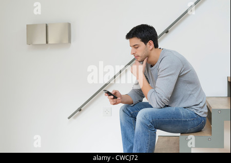 Uomo seduto sulle scale utilizzando un telefono cellulare Foto Stock