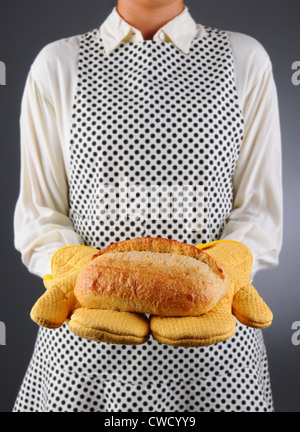 Primo piano di una massaia in un grembiule e guanti da forno tenendo un sfornato fresco della pagnotta di pane. Foto Stock
