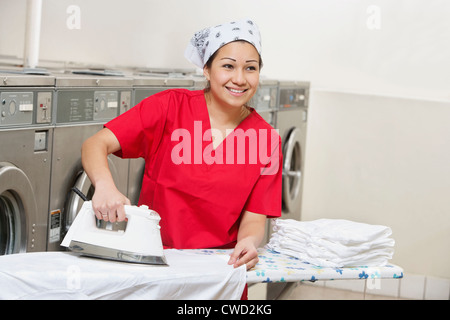 Felice giovane dipendente bandana da indossare durante la stiratura in lavanderia a gettoni Foto Stock