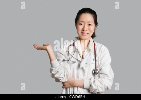 Ritratto di una donna asiatica medico la visualizzazione di un prodotto invisibile su sfondo grigio Foto Stock