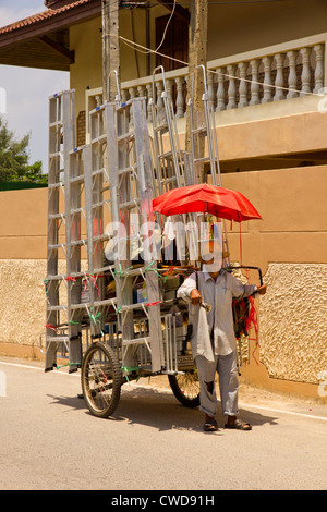 Un uomo tailandese la vendita di scale di alluminio da un due ruote carrello. Foto Stock