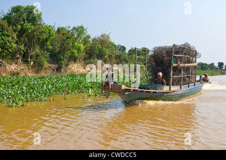 Vista orizzontale di un giovane ragazzo seduto sulla prua di una barca da pesca riportando un sacco di reti vuote e pentole in Kompong Khleang, Cambogia Foto Stock