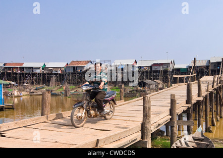 Vista orizzontale di un uomo alla guida di un ciclomotore attraverso un malsicuro vecchio ponte di Kompong Khleang villaggio galleggiante, in Cambogia. Foto Stock