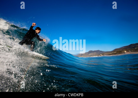 Un surfista maschio imposta per una camera sul retro mentre navigano a Zuma Beach in Malibu, California. Foto Stock