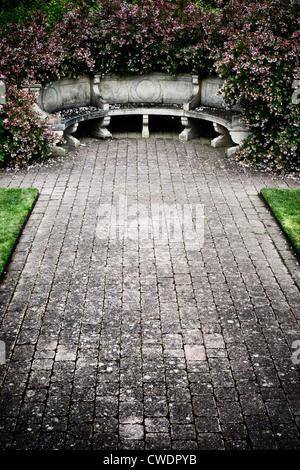 Posti a sedere in pietra circondato da Abelia x grandiflora in Penelope Hobhouse giardino alla RHS Wisley Gardens. Vintage filtro applicato Foto Stock