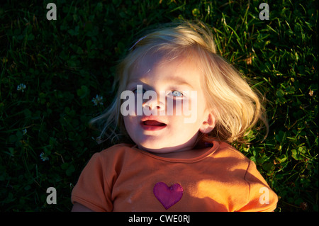 Un allegro bionda bambina giacente in erba rendendo divertente Foto Stock