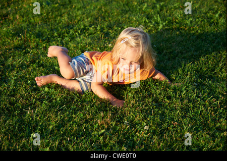 Un allegro bionda bambina giacente in erba rendendo divertente Foto Stock