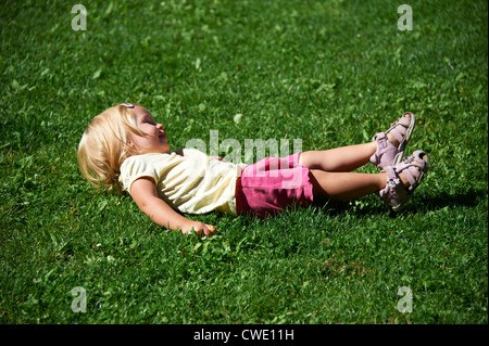 Un allegro bionda bambina giacente in erba rendendo divertente Foto Stock