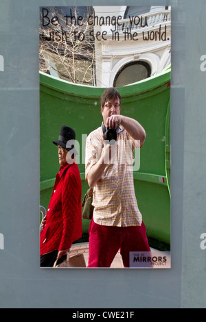 Self-portrait del fotografo in un specchio di distorsione (SF specchi Progetto) con una donna orientale passato a piedi in un rivestimento di colore rosso Foto Stock
