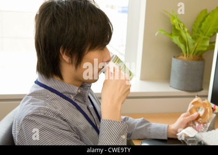 Imprenditore in abbigliamento casual bere alla scrivania Foto Stock