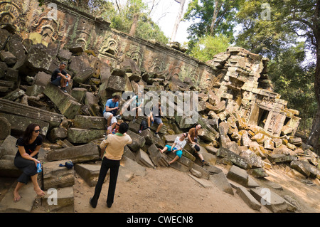 Vista orizzontale di turisti che si siedono sulle rovine di una parete con una guida turistica a Ta Prohm o Tomb Raider tempio di Angkor Thom. Foto Stock