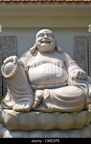 Verticale fino in prossimità di un grasso ridendo statua del Buddha scolpita in marmo in una giornata di sole. Foto Stock