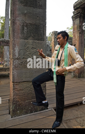 Verticale di chiusura del tour guida dimostrando apsara mosse di danza sulla storica bassorilievi presso il tempio Bayon, Angkor Thom. Foto Stock