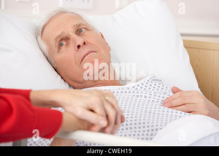 Senior uomo nel letto di ospedale azienda moglie per la mano Foto Stock