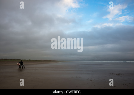 Un giovane con le loro tavole da surf sulla spiaggia di pollice Strand (di Ryan alla figlia di fama), la penisola di Dingle, nella contea di Kerry, Irlanda. Foto Stock