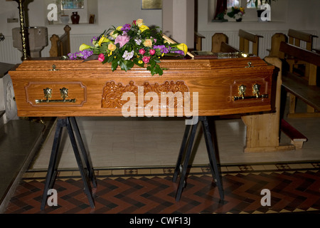 Una bara di legno con l'ultima cena il design e i fiori sulla sommità appoggiata nella chiesa pronto per l'occupante i funerali il giorno seguente Foto Stock