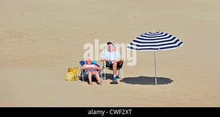 Anziani lucertole da mare dormire in sedie da spiaggia accanto all ombra del parasole e ottenere le scottature solari in estate lungo la costa del Mare del Nord Foto Stock