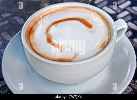 Primo piano di una tazza bianca e piattino con caffè latte ha la lettera C dribbled in schiuma per un tipo di caffè art. Caldissimo. Foto Stock