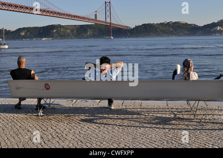 Gente seduta sul banco da parte del fiume Tago a Lisbona, Portogallo Foto Stock