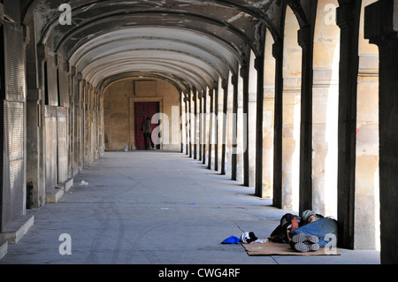 Parigi, Francia. Place des Vosges. L'uomo addormentato sotto il porticato Foto Stock