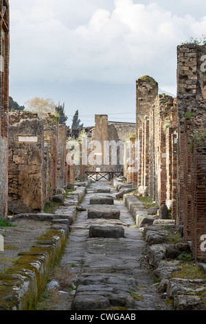 Vista lungo Vicolo di Eumachia, una strada stretta nella città romana di Pompei, lastricata in basalto con pietre miliari attraverso Foto Stock