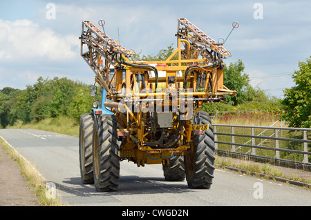 Attrezzatura di irrorazione del prodotto montata su un trattore largo che viaggia lungo una strada rurale stretta Essex Inghilterra UK Foto Stock