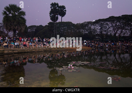 Vista orizzontale di turisti che si siedono insieme intorno ad un lago di guardare il tramonto su Prasat Angkor Wat. Foto Stock