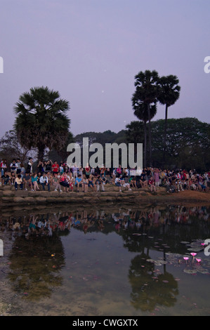 Vista verticale di turisti che si siedono insieme intorno ad un lago di guardare il tramonto su Prasat Angkor Wat. Foto Stock