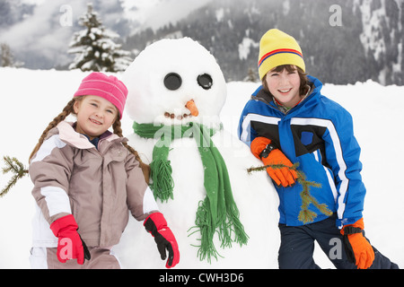 Due giovani bambini edificio pupazzo di neve sugli sci vacanze in montagna Foto Stock