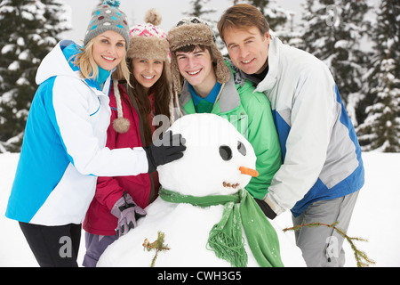 Famiglia di adolescenti edificio pupazzo di neve sugli sci vacanze in montagna Foto Stock