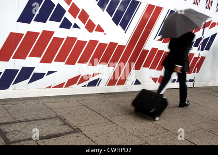 Uomo con una valigia passando una grande Unione bandiera nel centro di Londra Foto Stock