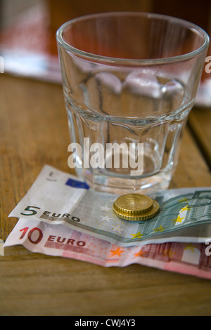 Bicchiere vuoto e di banconote e monete in euro Foto Stock