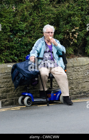 Signora anziana sulla mobilità scooter godendo di un gelato durante il giorno fuori Foto Stock