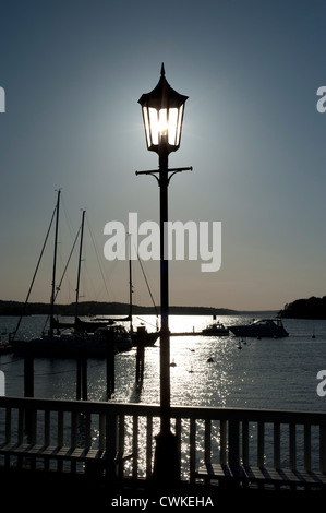 Sun lighting fino alla luce di una lampada posta in un porto con barche in background Foto Stock