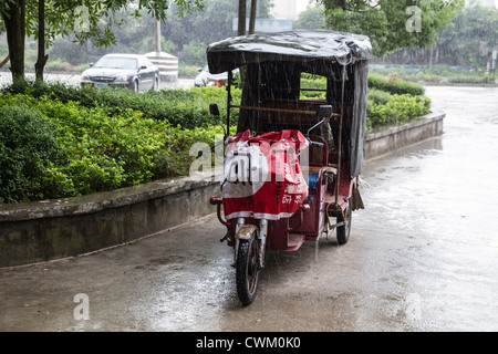 Electric pedicab taxi sotto la pioggia Foto Stock